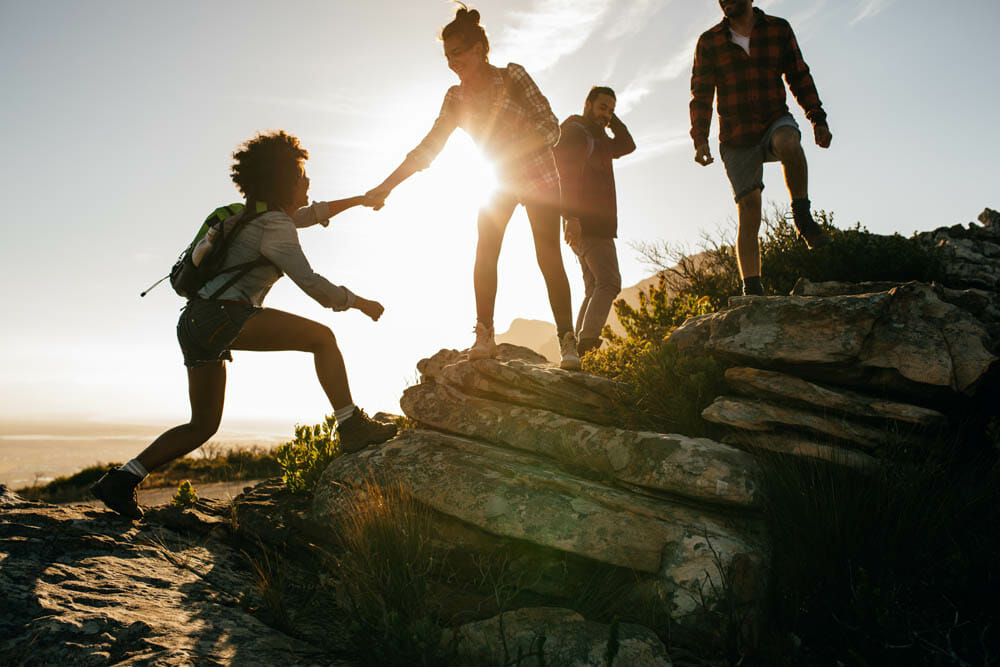 Group of hikers on a mountain. Woman helping her friend to climb a rock. Young people on mountain hike at sunset.